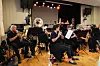Et korps sitter og spiller i et lokale med noter, instrumenter og sceneutstyr.