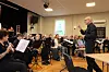 Dirigent leder et orkester som øver i en sal med musikere, noter og instrumenter.