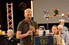 En mann spiller et blåseinstrument foran et notestativ under en innendørs musikkopptreden.
