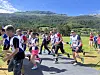 Flere løpere i sportsdrakter beveger seg langs en sti med fjell og skog i bakgrunnen.