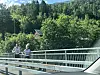 To personer jogger på en bro med grønn skog og en liten bygning i bakgrunnen.
