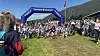 Stor gruppe mennesker samlet ved en blå målportal i et grønt fjellandskap.