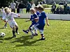 Barn spiller fotball på en gressbane med tilskuere i bakgrunnen.