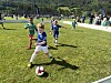 Barn spiller fotball på gress med tilskuere i bakgrunnen.