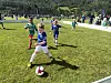 Barn spiller fotball på gress med tilskuere i bakgrunnen.