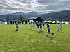 Ungdommer spiller fotball på en gressbane med fjell og skyer i bakgrunnen.
