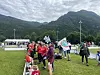 Folk samles på en gresslette med flagg, telt og fjell i bakgrunnen.