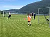 Barn og voksne på en fotballbane med mål, kjegler og fjell i bakgrunnen.