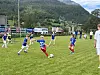 Ungdommer spiller fotball på en gressbane foran skogkledde fjell.