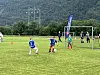 Ungdommer spiller fotball på en gressbane med mål, kjegler og skogkledde fjell bak.