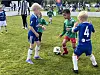 Tre barn i fotballdrakter kjemper om en ball på en gressbane.