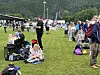 Folk sitter og står på et gressfelt under et utendørsarrangement med fjellskråning i bakgrunnen.