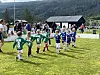 Barn spiller fotball på en gressbane med tilskuere og fjell i bakgrunnen.