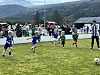 Barn spiller fotball på en gressbane foran publikum og fjell i bakgrunnen.