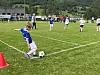 Barn i blå fotballdrakt skyter på ballen ved en rød kjegle på en gressbane.