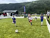 Barn spiller fotball på en gressbane med fjell og skog i bakgrunnen.