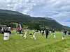 Barn og voksne leker og trener på en gresslette med fjellandskap bak.