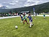 Barn spiller fotball på en gressbane med fjell i bakgrunnen.