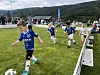 Barn spiller fotball på en gressbane mens publikum følger med langs banen.