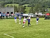 Flere ungdomsspillere i blått og hvitt spiller fotball på en grønn gressbane.