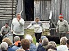 Fire skuespillere opptrer foran en låve, med publikum samlet foran scenen.