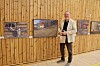 En mann står foran en vegg med flere innrammede bilder i et rom med trepanel.