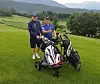 To golfspillere står med golftraller på en gresskledd golfbane med fjell i bakgrunnen.