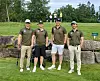 Fire golfspillere står side om side foran store steiner i en park.