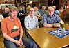 Tre menn sitter rundt et bord i en kafé med rustikk innredning.