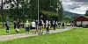 Ei gruppe mennesker står samla på tunet ved Austigard Børset med bygninger, vei og fjell i bakgrunnen.