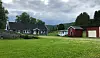 Gårdstun med hus, rødt uthus og garasje ved Børsettrøa, omgitt av gress og trær.