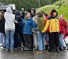 En gruppe ungdommer står på en våt parkeringsplass i regnvær.