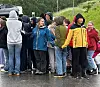 En gruppe ungdommer står på en våt parkeringsplass i regnvær.