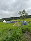 Flere telt står på en gresslette med åser og grå himmel i bakgrunnen.