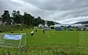 Et fotballmål på en gressbane med flere personer og telt i bakgrunnen under overskyet himmel.