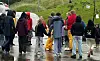 Personer står samlet på en våt vei ved en grønn bakke i regnvær.