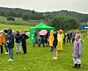 Folk i regnklær står spredt på et grasfelt ved grønne telt i regnvær.