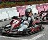 Gokartfører i hjelm sitter i en svart-rød kart merket med nummer 2 foran plastbarrierer.