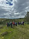 Gruppe turgåere står på en gresskledd ås under dramatisk skydekke.