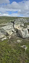 Store steinblokker i et åpent, grønt fjellandskap med skyet himmel.