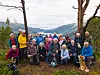 En gruppe mennesker står samlet utendørs på en sti med fjellandskap og fjord bak seg.
