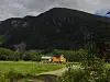 Gult hus i et grønt fjellandskap med sti, trær og noen mennesker i nærheten.