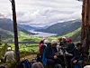 Turgåere sitter ved et utsiktspunkt med utsikt over en grønn dal og fjellandskap.