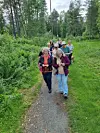 En gruppe mennesker går på en smal sti gjennom en grønn skog.