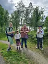 Fire personer står på en sti ved skogkanten med trær og gress rundt seg.