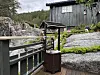 Pyntebrønn, trebygning med grå kledning, berg, dekorative figurer, grønne planter.