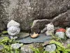 Små dekorative figurer står på steinheller foran berg eller stor stein.