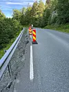 Varselmarkører står langs kanten av en smal vei ved en skogkledd fjellside.