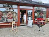 Butikkfasade med store vinduer, utstilte figurer og et rødt brettstativ på fortauet.