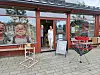 Butikkfasade med store vinduer, utstilte figurer og et rødt brettstativ på fortauet.